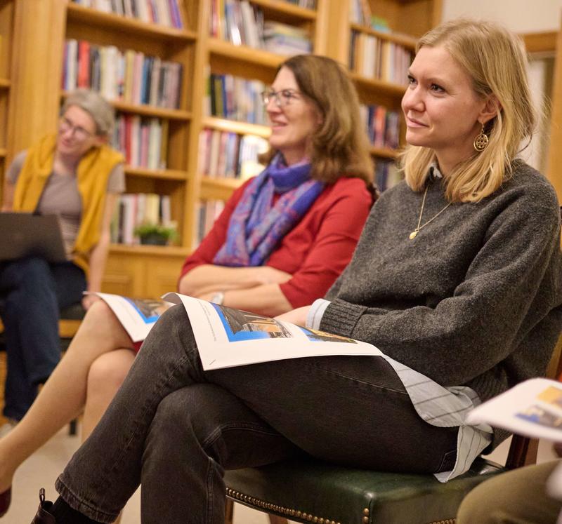 Three women sit on chairs listening to someone speak