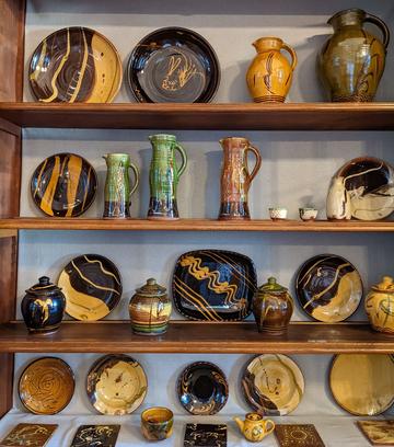 Bowen Four shelves of studio pottery on display with a range of shapes from tiles to jugs to large plates