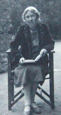 Black and white photograph of a female.  Figure seated in a chair reading a book. 
