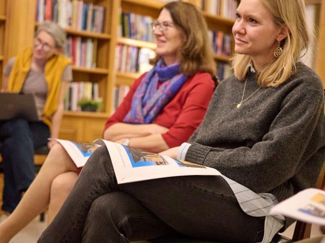 Three women sit on chairs listening to someone speak