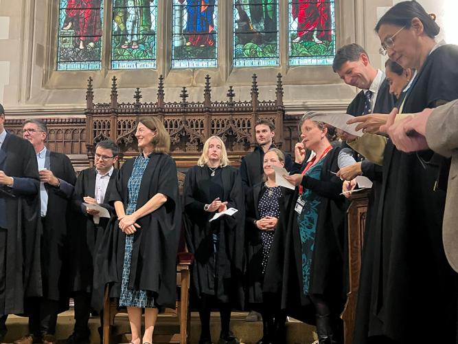 A group of people in academic gowns surround Principal Beth Breeze in the College Chapel