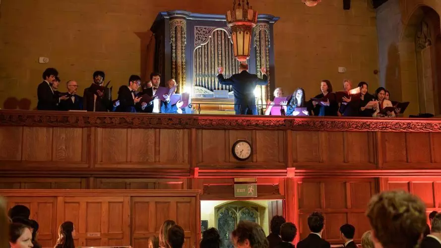 Choir singing from gallery in Arlosh Hall with organ in background