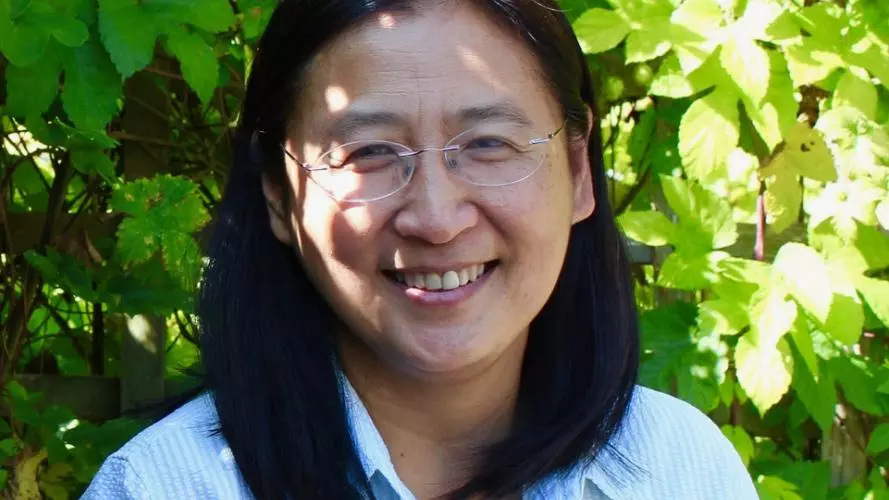 Photo portrait of Professor Bee Wee, smiling against a backdrop of green foliage