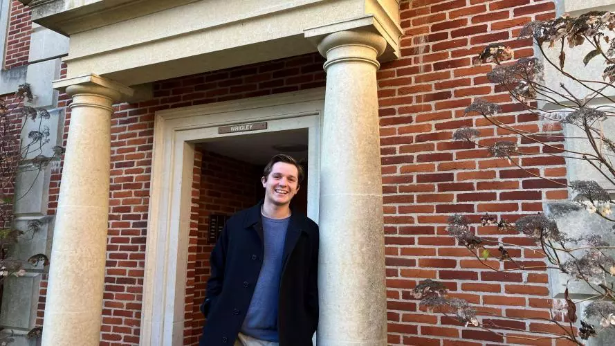 A young man leans against the column of a red-brick building