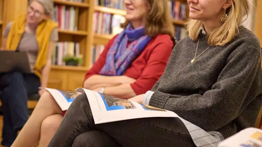 Three women sit on chairs listening to someone speak