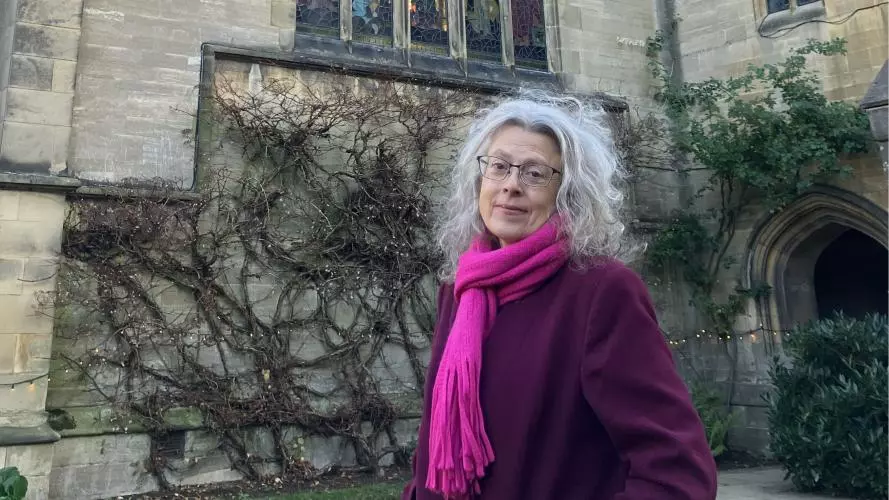 Woman in a coat standing in college quad in front of chapel