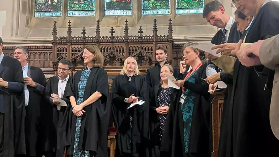 A group of people in academic gowns surround Principal Beth Breeze in the College Chapel