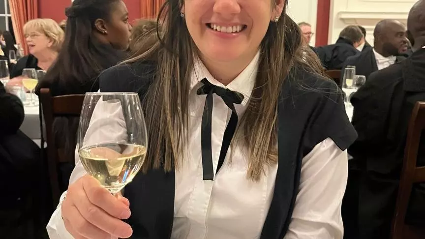 A woman in academic gown drinking a glass of wine