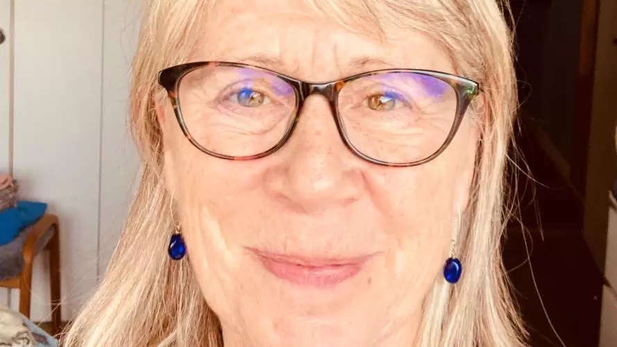 Portrait photo of Claire MacDonald. Claire wears glasses, blue drop earrings and has long hair. She is smiling directly at the viewer. 