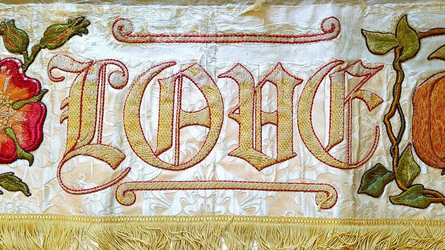 Embroidered piece of cloth showing the word Love as well as two flowers and some foliage