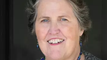 Maureen Oneill wearing blue earrings and necklace, posing in front of a black background.