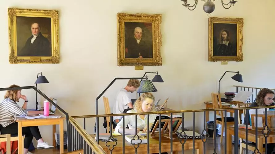 A photo with several students sitting by the desks on the upper level of the Tate Library, revising.