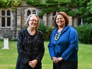 The Principal and Anna Deavere Smith smiling together in the Tate Quad. In the background, stonework, grass and green foliage
