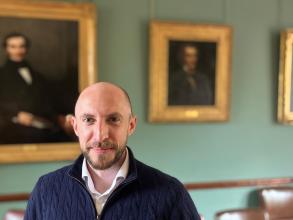 Joe Dollin posing in front of the portraits in the HMC Senior Common Room