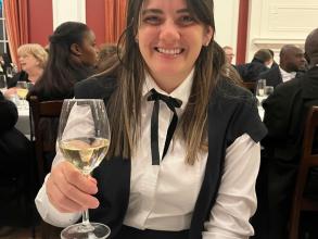 A woman in academic gown drinking a glass of wine