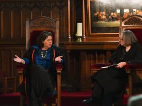 The Principal and Anna Deavere Smith are seated together in high-backed chairs at the front of the Chapel. Anna is on the left, gesturing as she explains a point, while the Principal (on the right) listens attentively. 