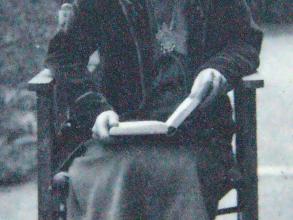Black and white photograph of a female.  Figure seated in a chair reading a book. 