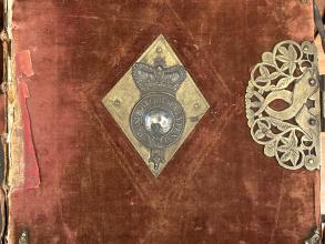 An elaborate cover with metal corners and central crest on a pink velvet background