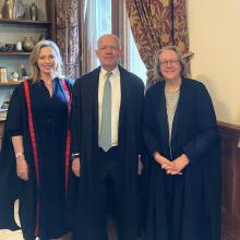 Three people, two women, one man in the centre, pose in academic gowns in a wood-panelled room
