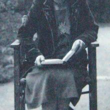 Black and white photograph of a female.  Figure seated in a chair reading a book. 