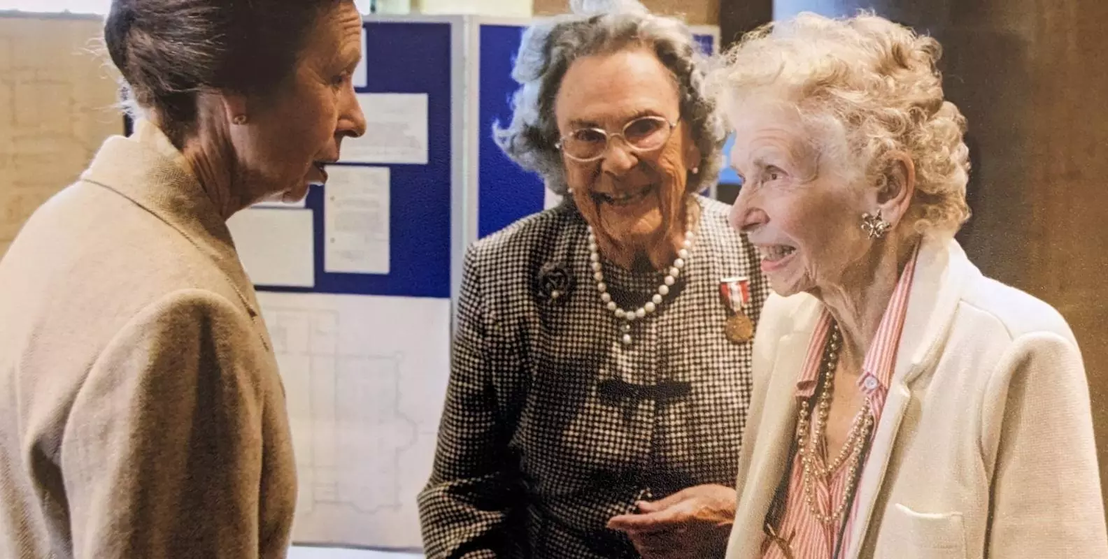 A group photograph of three figures talking.  Princess Anne is pictured on the right chatting to two ladies who are smiling. 